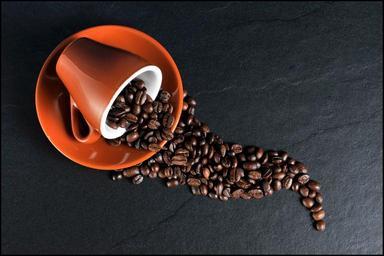 An espresso cup on its side with coffee beans spilling from it in the shape of a river.